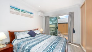 Un dormitorio con cama, mesitas de noche, ventana con cortinas y vistas al exterior.