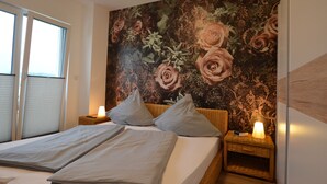 A bedroom with a large floral tapestry on the wall, a bed with two pillows, and a bedside table with a lamp. - Spacious holiday home with sauna, mountain view and garden in Lechbruck am See (Lechbruck)