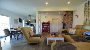 A living room with a sofa, armchair, coffee table, and a red bookshelf. - Spacious holiday home with sauna, mountain view and garden in Lechbruck am See (Lechbruck)