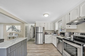 A modern kitchen with white cabinets, stainless steel appliances, and a marble countertop.