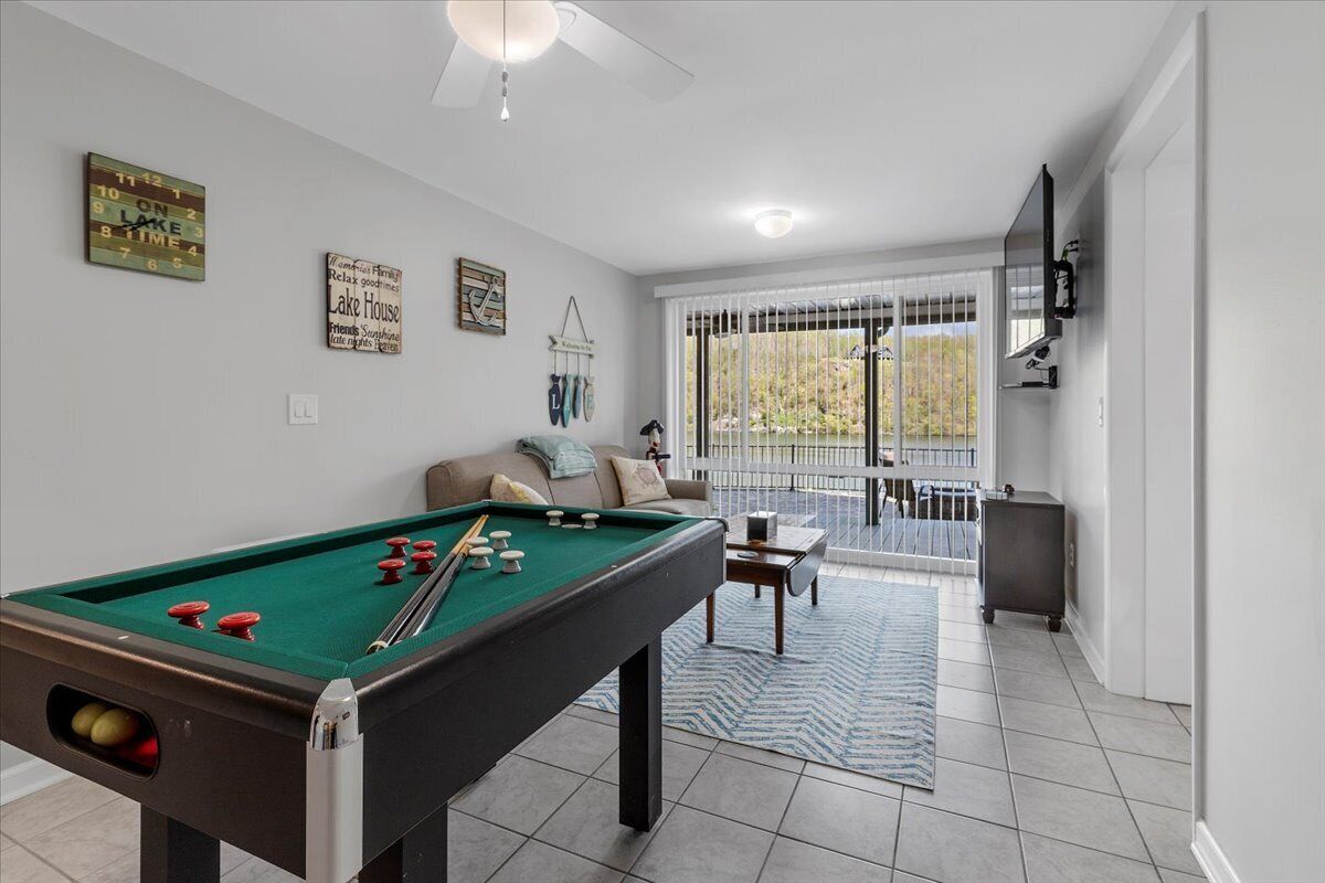 A pool table in a room with a sofa, a television, and a view of a balcony with a railing.