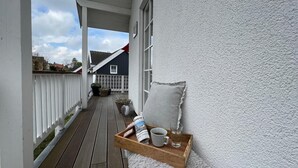 Eine Holzterrasse mit weißer Geländer, ein gemütlicher Sitzbereich mit Kissen und einem Tablett mit Tasse und Glas.