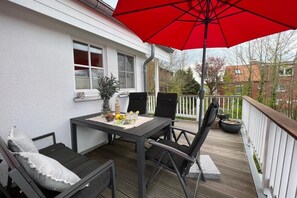 A deck with a table and chairs, a red umbrella, and a potted plant.