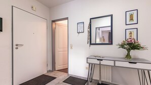 Een gang met een witte deur, een witte radiator, een spiegel en een bloemenvaas op een console tafel.
