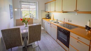 Een moderne keuken met een eethoek, met een groot raam, houten kastjes en een inbouwoven.