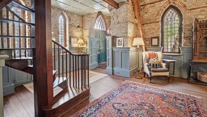 A spacious room with a wooden staircase, stone walls, and large windows. - Incredible Coastal Castle on Sullivans Island (Sullivans Island)