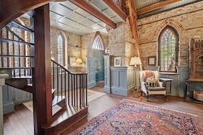 A spacious room with a wooden staircase, stone walls, and large windows. - Incredible Coastal Castle on Sullivans Island (Sullivans Island)