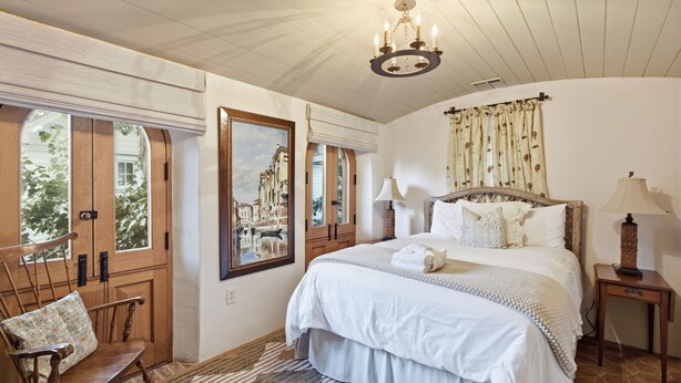 A bedroom with a large bed, a wooden chair, a nightstand, a lamp, and a painting on the wall. - Incredible Coastal Castle on Sullivans Island (Sullivans Island)