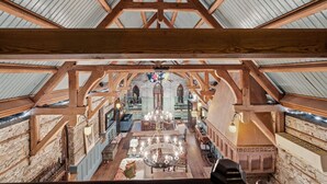 An interior with a high ceiling, wooden beams, stone walls, and a central chandelier. - Incredible Coastal Castle on Sullivans Island (Sullivans Island)