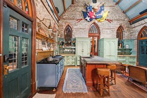 A traditional kitchen with stone walls, wooden cabinets, and a large window. - Incredible Coastal Castle on Sullivans Island (Sullivans Island)