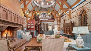 A spacious room with a high ceiling, exposed wooden beams, a fireplace, and a cozy seating area with multiple chairs and a table. - Incredible Coastal Castle on Sullivans Island (Sullivans Island)