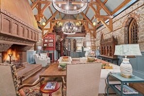 A spacious room with a high ceiling, exposed wooden beams, a fireplace, and a cozy seating area with multiple chairs and a table. - Incredible Coastal Castle on Sullivans Island (Sullivans Island)