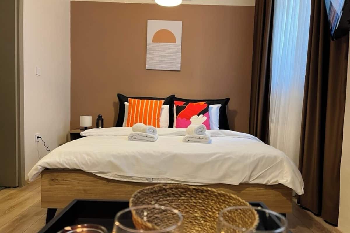A hotel room with a bed, pillows, a bedside table, a lamp, a tray with candles, and a wall art piece.