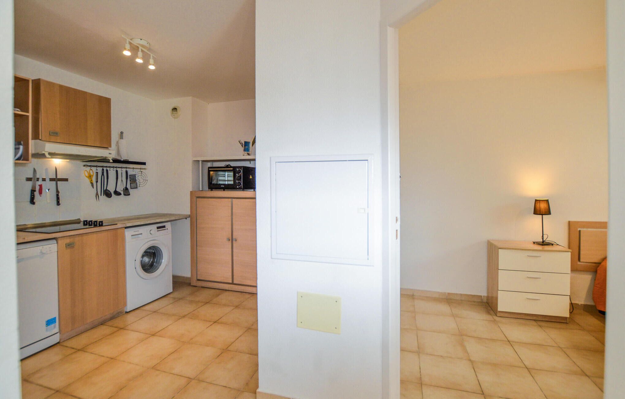 A compact kitchen with a washing machine, wooden cabinets, and a microwave.