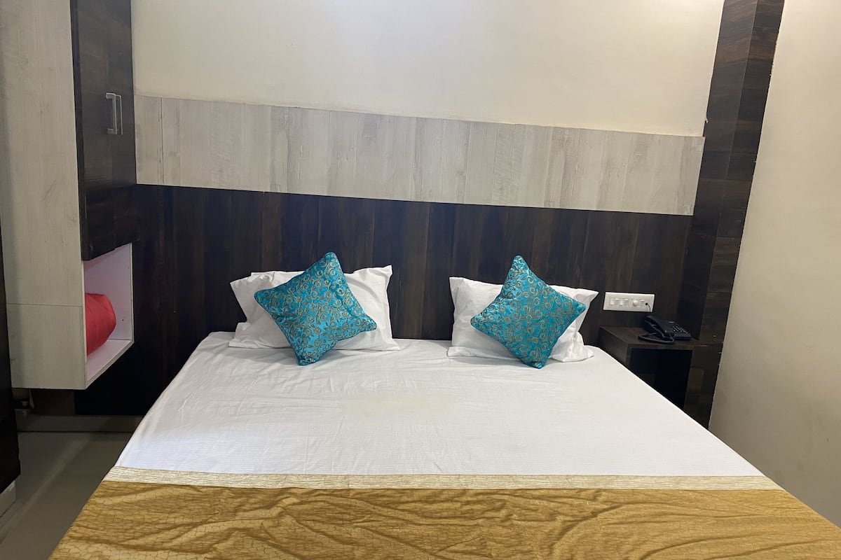 A neatly made bed with two patterned pillows, a wooden headboard, and a bedside table with a phone.