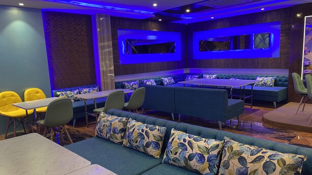 A modern restaurant interior with blue and green seating, marble tables, and blue ambient lighting. - Hotel Brij Residency (Bhopal)