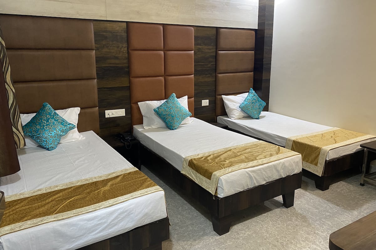 A hotel room with three single beds, each with a brown headboard and white bedding. The room has a modern design with a wooden accent wall and a small table with a tablecloth.