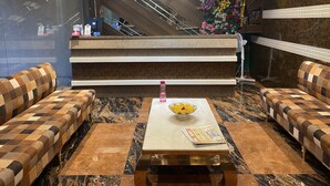 A lobby with checkered sofas, a marble coffee table, a reception desk, and an escalator. - Hotel Brij Residency (Bhopal)