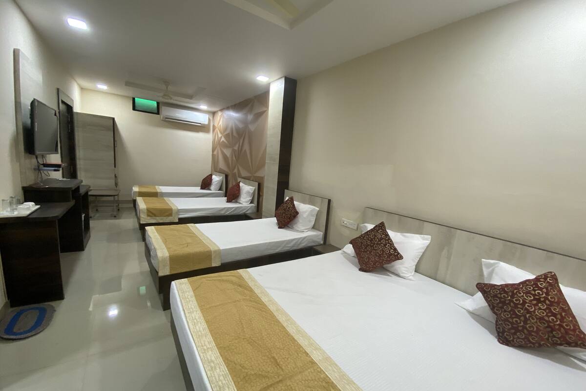 A hotel room with three single beds, a desk, a chair, a television, and an air conditioning unit.