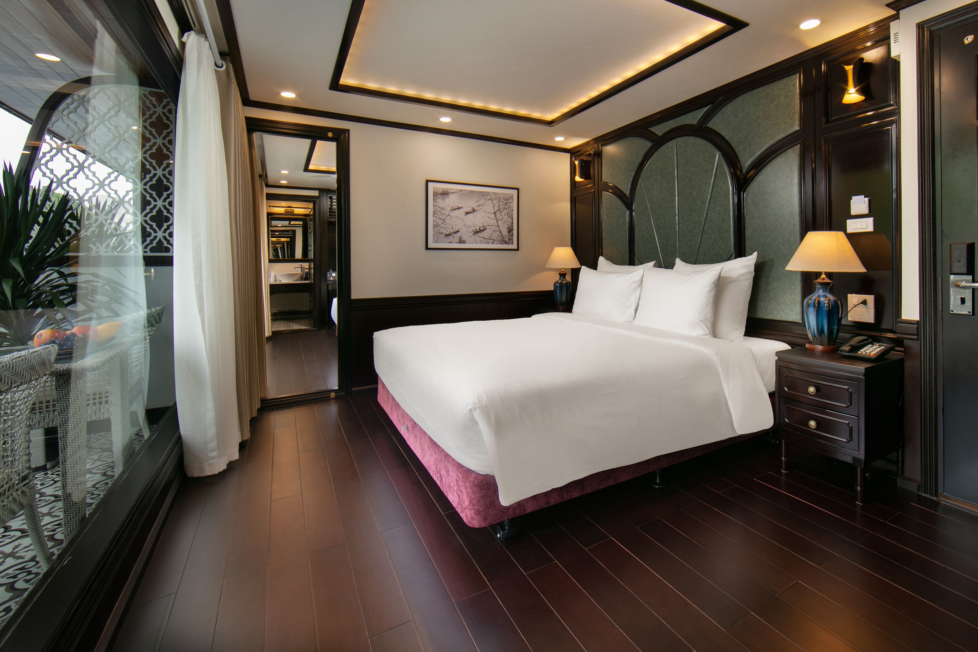 Une chambre d’hôtel moderne avec un grand lit, des lampes de chevet, une table de nuit et une vue sur l’extérieur, visible à travers une porte vitrée.