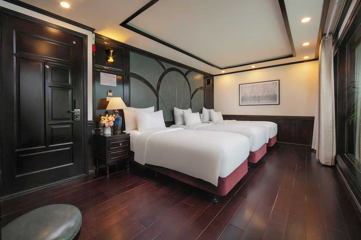 Una habitación de hotel con una cama grande, una mesita de noche con lámpara y una puerta de madera oscura.