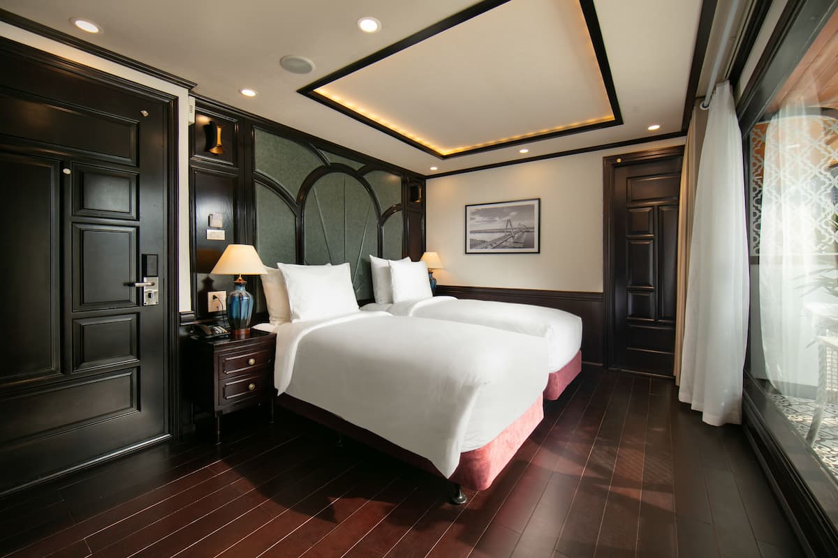 Una habitación de hotel con una cama grande, una mesita de noche, una lámpara y un ventanal con cortinas.
