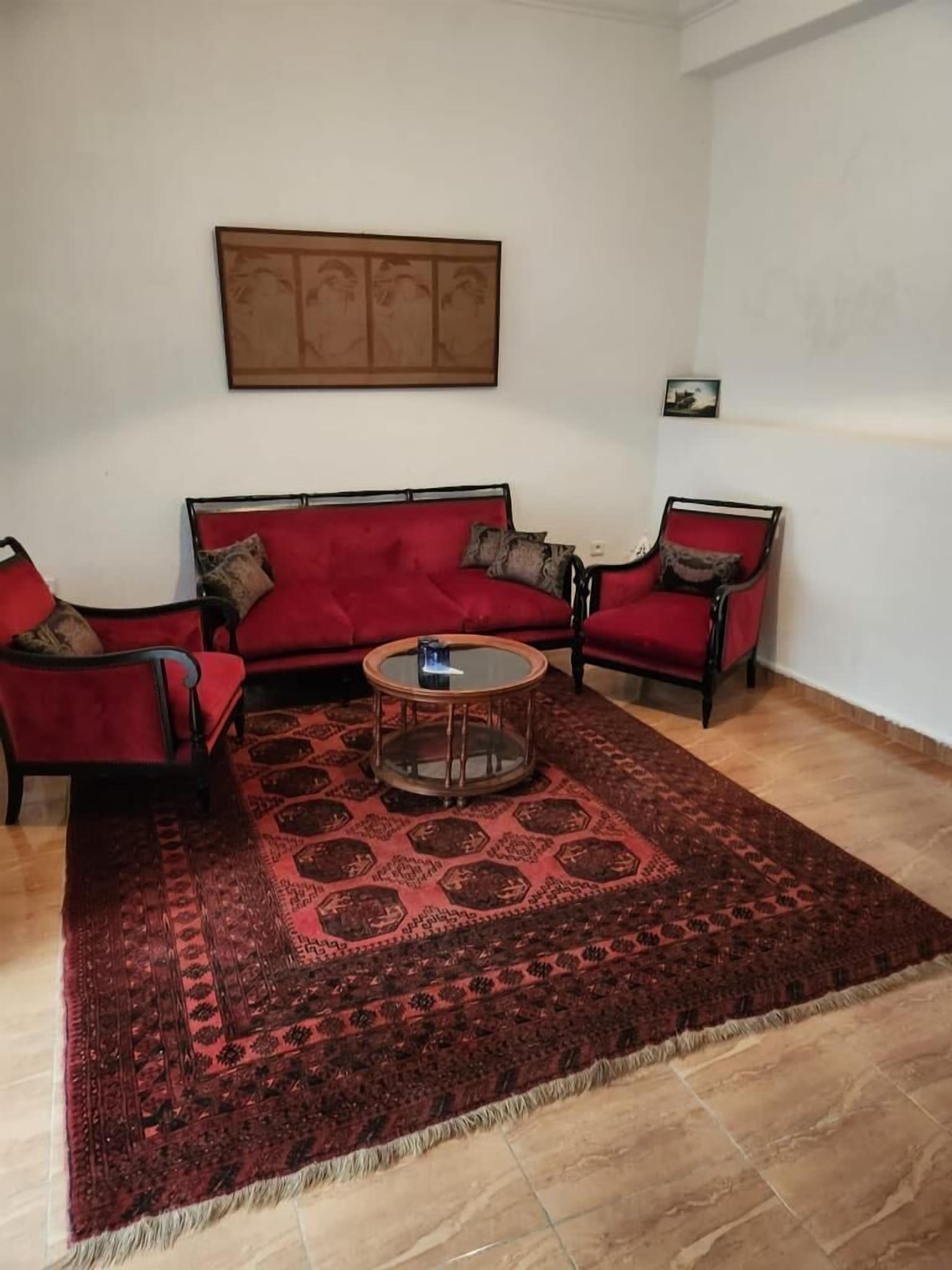 A living room with a red sofa, two armchairs, a coffee table, and a patterned rug.