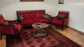 A living room with a red sofa, two armchairs, a coffee table, and a patterned rug.