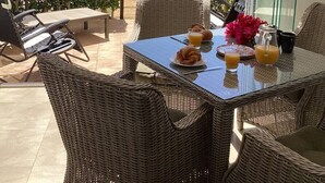 Un patio con muebles de mimbre, una mesa dispuesta con cruasanes, jugo de naranja y una jarra.