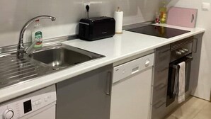 Una cocina compacta con muebles grises, lavavajillas, lavadora, tostadora y horno pequeño.
