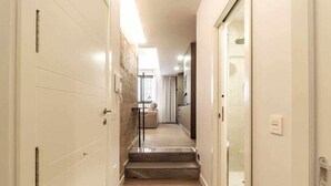 A narrow hallway with a wooden floor, a set of stairs leading to a room, and a door on the right.