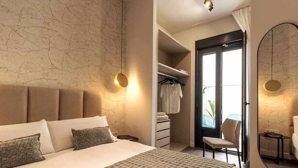 A bedroom with a large bed, a wardrobe, a mirror, and a view of the outside.