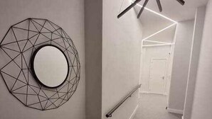 A modern hallway with a geometric wall art piece, a round mirror, and a bench.