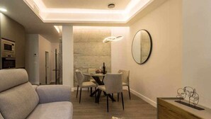 A modern living room with a sofa, a dining area with a table and chairs, and a kitchen in the background.
