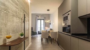 Una cocina moderna con electrodomésticos integrados, un comedor con mesa y sillas, y un pasillo con una planta y un vaso de jugo de naranja sobre una consola.