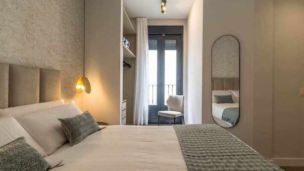 Un dormitorio con una cama grande, una lámpara de noche, un espejo y vistas a un balcón.