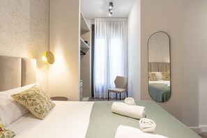 Una habitación de hotel con cama, una silla, un espejo y un armario.