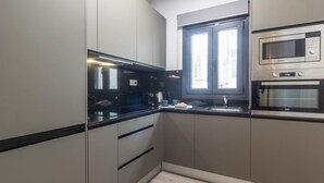 Een moderne keuken met een zwart aanrecht, roestvrijstalen apparatuur en een raam met jaloezieën.