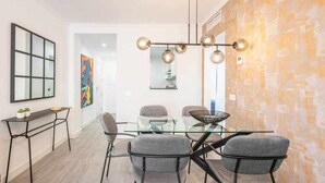 Una zona de menjador moderna amb taula de vidre, cadires tapissades de gris i una lluminària de suspensió esfèrica i singular.