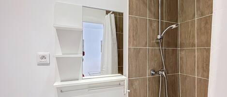Un baño moderno con un lavamanos blanco, un espejo y una ducha con cabezal de ducha manual.