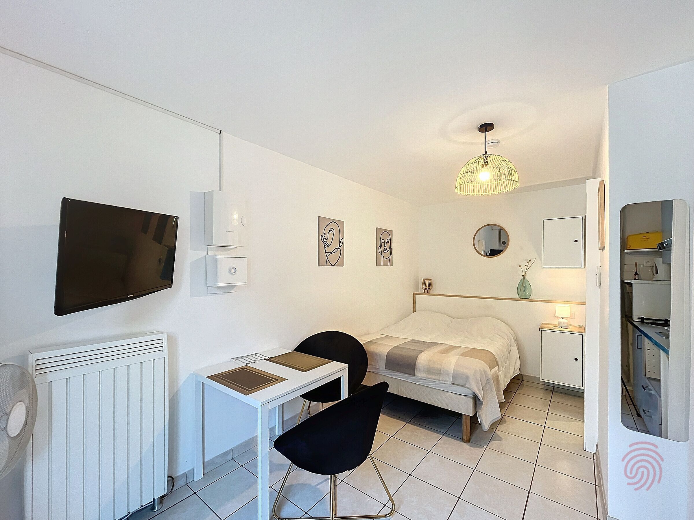 Une petite pièce propre, comprenant un lit, un bureau, une chaise, un téléviseur, un radiateur, une lampe et un miroir.