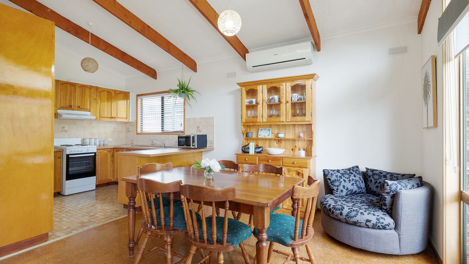 A compact kitchen with wooden cabinets, a dining table with chairs, and a built-in seating area with a sofa.