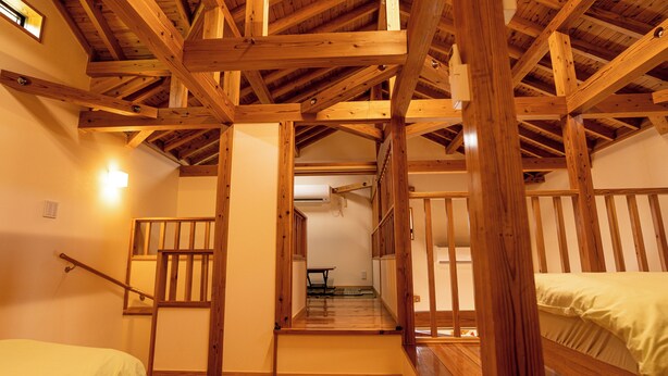 Interior de madera con una escalera que sube a un segundo piso, una cama en la planta baja y una lámpara en la pared.