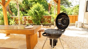 Un patio al aire libre con una mesa de madera, una parrilla y un suelo de baldosas de piedra.