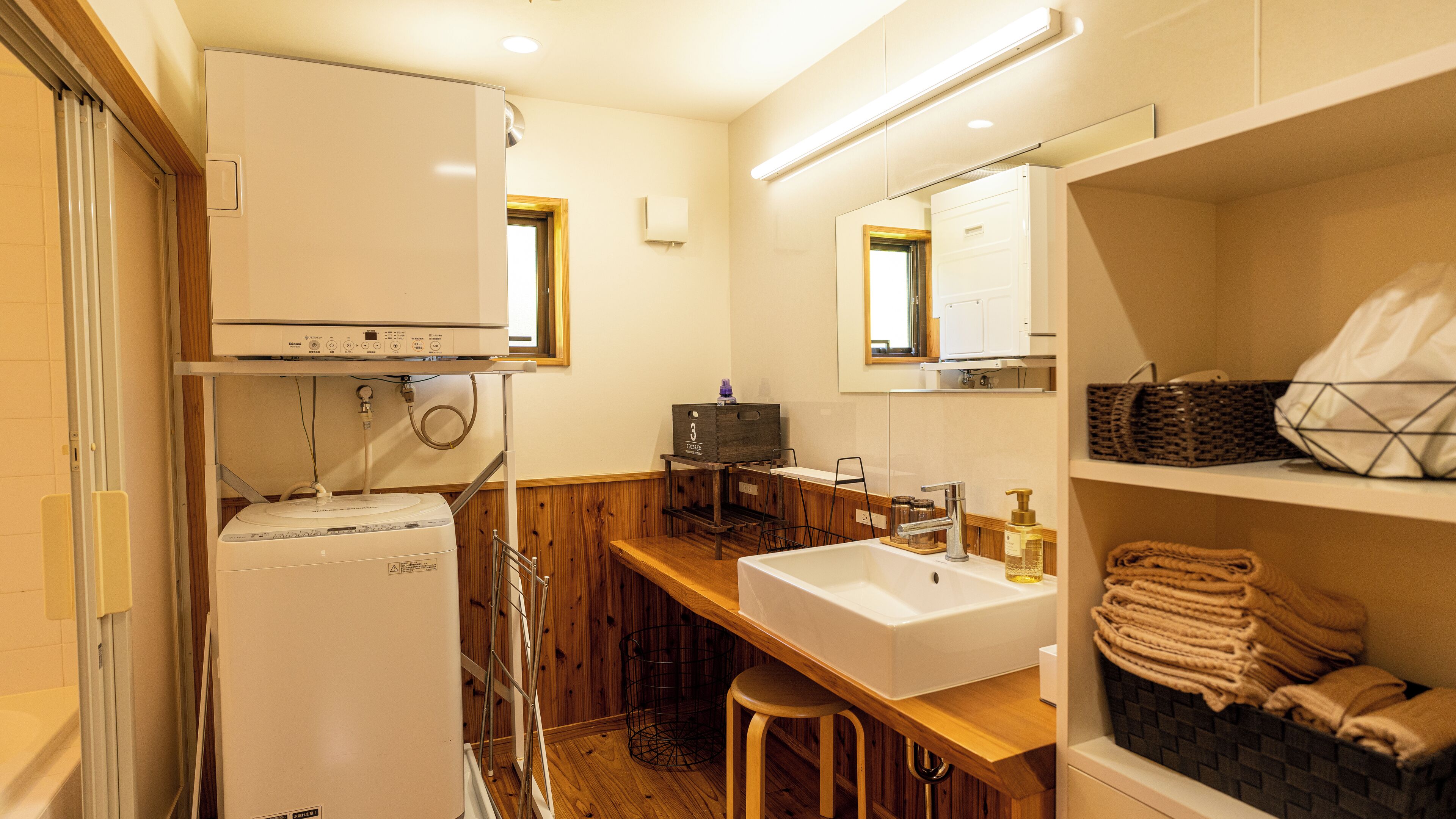 Une petite salle de bain avec un lavabo blanc, un miroir, un tabouret en bois et un porte-serviettes.