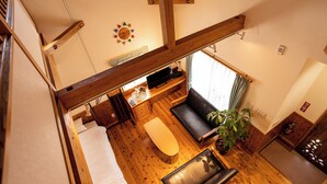 Una habitación con techo de madera, una cama, un escritorio con una computadora, un sofá, una planta en maceta y un pequeño santuario.