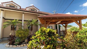 Edificio residencial con un patio cubierto, rodeado de plantas variadas y un pequeño jardín.