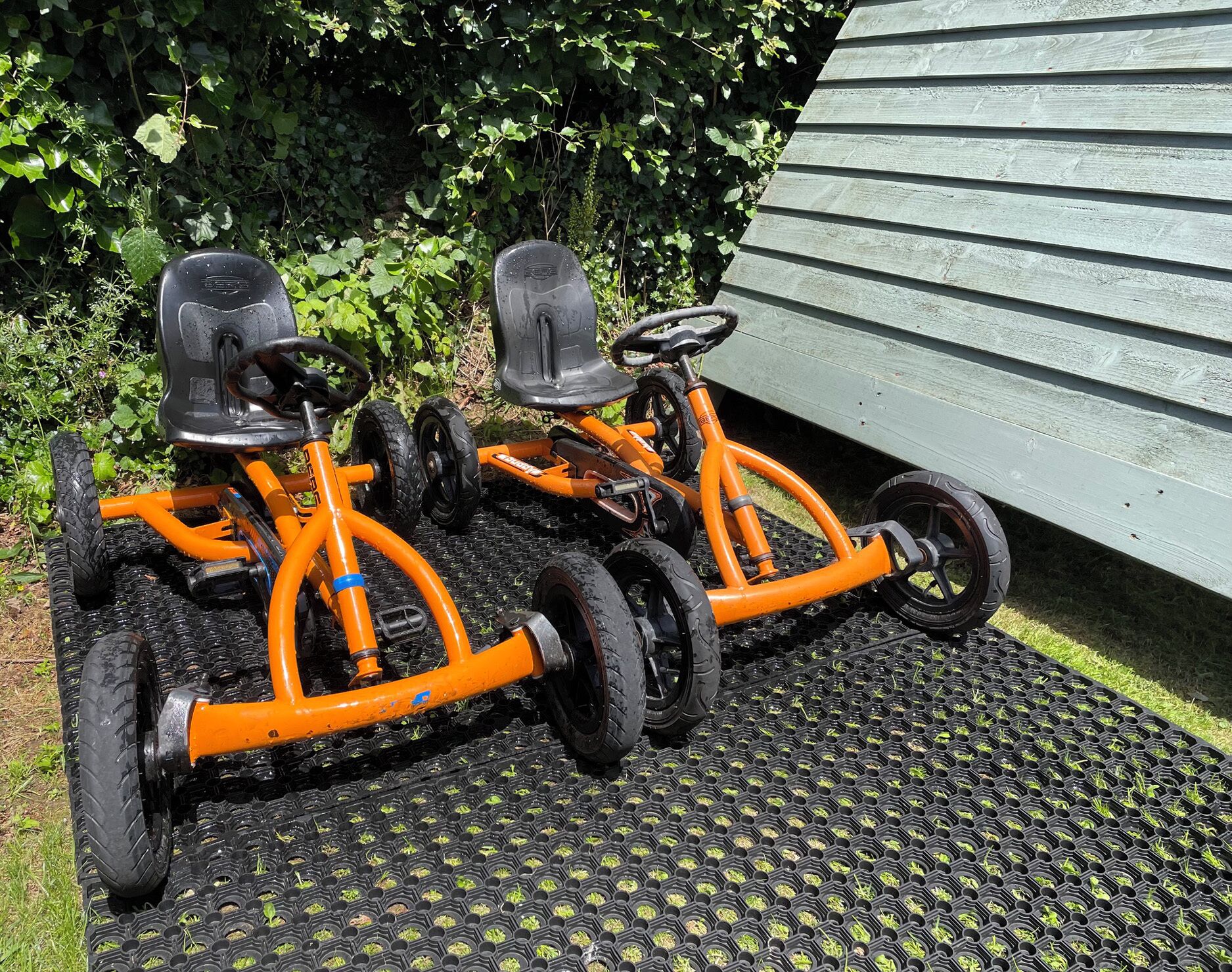 Two orange tricycles parked on a black rubber mat.