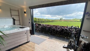 A spa room with a hot tub, exercise bike, and a view of a green field. - Ashlea (Launceston)