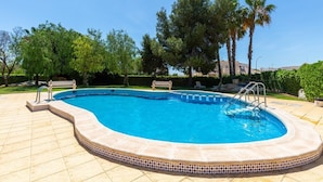 A swimming pool with a tiled edge, surrounded by a patio area with a bench and a palm tree. - GoldenCore by Fidalsa (Orihuela)